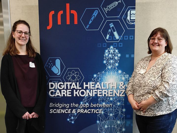 Leevke Wilkens (rechts) und Miriam Bursy (rechts) stehen vor einem Roll-Up der Digital Health & Care Konferenz 