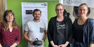 Auf dem Bild sind vier Personen zu sehen, die in einem Raum stehen. Sie lächeln und posieren gemeinsam vor einer grünen Wand, die mit Informationen über die Nutzung von Virtual-Reality-Technologie versehen ist. Eine der Personen hält eine VR-Brille in den Händen. Im Hintergrund ist ein Banner des CJD (Christliches Jugenddorfwerk Deutschlands) sichtbar, das auf Bildungs- und Sozialangebote hinweist. Die Atmosphäre wirkt freundlich und kooperativ, was auf eine Veranstaltung oder einen Workshop hindeutet, der sich mit innovativen Technologien beschäftigt.
