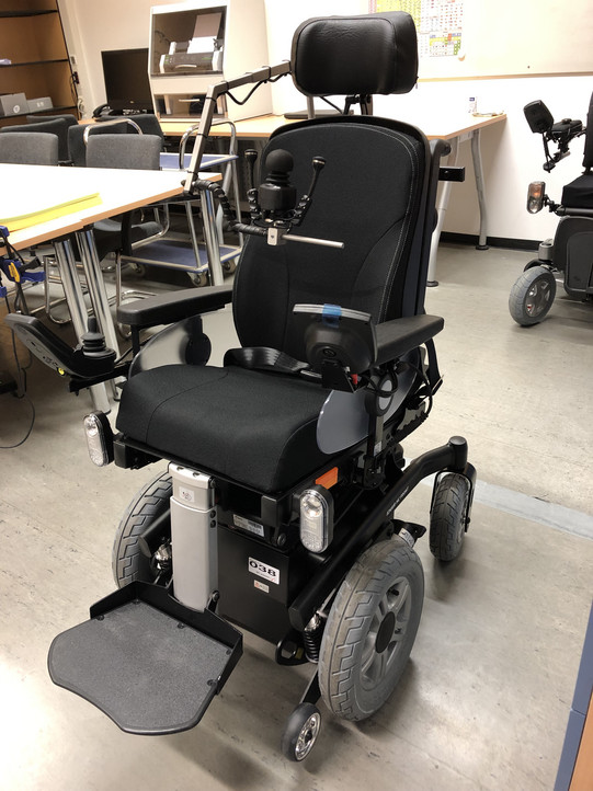 Ein elektrischer Rollstuhl mit verschiedenen Steuerungshilfen, wie ein Joystick und eine Kinnsteuerung