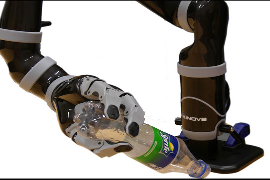 Ein Roboterarm hält mit drei Fingern eine Plastikflasche fest. Der lange Arm ist an einer Montageplatte befestigt.