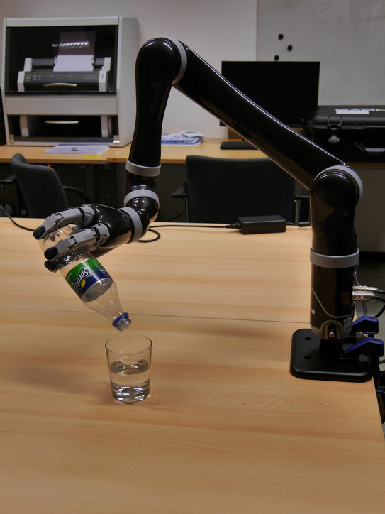 Ein Roboterarm schenkt Sprite in ein Glas auf einem Tisch ein. Der Arm ist an der Tischplatte befestigt. 