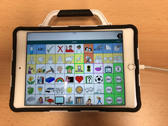Talker Prio 8 iPad mit Schutzhülle und Tragegriff. Auf dem Display sind verschiedene Symbole und ein Textfeld.