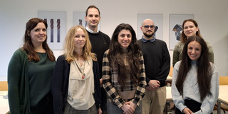 Sieben Personen stehen in einem Seminarraum nebeneinander und schauen in die Kamera.