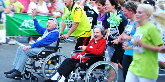 Ein Marathon. Es sind laufende Menschen und Menschen in Rollstühlen zu sehen.