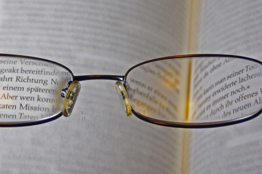 Durch eine Brille sieht man den Text eines aufgeschlagenen Buchs