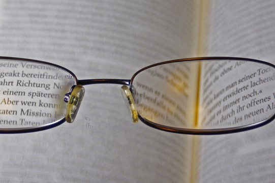Durch eine Brille sieht man den Text eines aufgeschlagenen Buchs