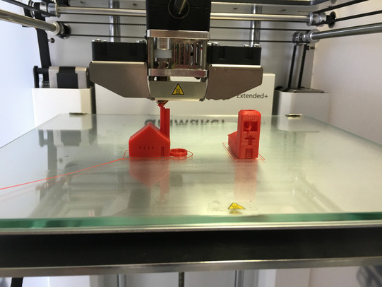 Der 3D-Drucker baut Schicht für Schicht zwei dreidimensionale Gebäudemodelle nebeneinander auf einer Platte auf.