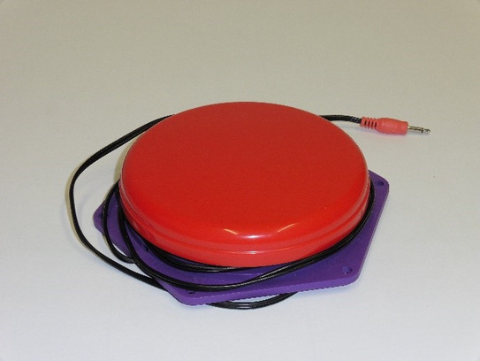 Eine rote Taste auf einer lilanen Bodenplatte. Ein Kabel ist um die Taste gewickelt.