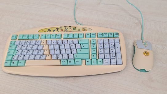 Eine bunte Tastatur mit besonders kleinen Tasten. Sie ist über ein Kabel mit einer gleichfarbigen kleinen Maus verbunden.