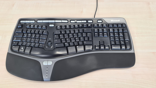 Gewölbtes Tastaturfeld, das durch einen Zoomregler in der Mitte geteilt wird. Die Tasten sind nach hinten geneigt. Es gibt eine Handballenauflage aus Kunstleder. Unterhalb der Leertaste ist eine Vor- und Zurücktaste. Oberhalb des Tastenfelds sind individuell programmierbare Zusatztasten. Die Tastatur ist an ein Kabel gebunden.