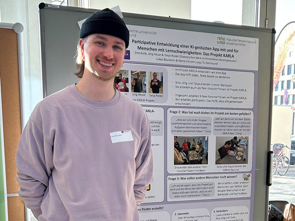 Das Bild zeigt Lukas Baumann, der vor dem aufgehängten Poster zum KARLA Projekt steht.