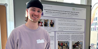 Das Bild zeigt Lukas Baumann, der vor dem aufgehängten Poster zum KARLA Projekt steht.