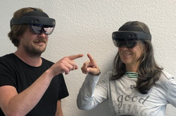 Eine weibliche und eine männliche Person, die eine HoloLens tragen und den Zeigefinger nach vorne ausstrecken