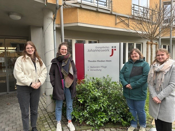 Foto von vier Mitarbeiterinnen des EVE4all-Projektes vor dem Theodor-Fliedner-Heim. Zwei Personen stehen jeweils rechts und links von einem Schild, auf dem steht: Evangelisches Johanneswerk, Theodor-Fliedner-Heim. 