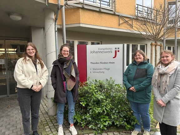 Foto von vier Mitarbeiterinnen des EVE4all-Projektes vor dem Theodor-Fliedner-Heim. Zwei Personen stehen jeweils rechts und links von einem Schild, auf dem steht: Evangelisches Johanneswerk, Theodor-Fliedner-Heim.