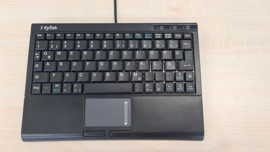 Mini-Tastatur mit integriertem Nummernblock im Tastenfeld. Unten ist ein Touchpad zum scrollen mit zwei Maustasten. Es gibt eine Handballenauflage. Die Tastatur ist an ein Kabel gebunden.