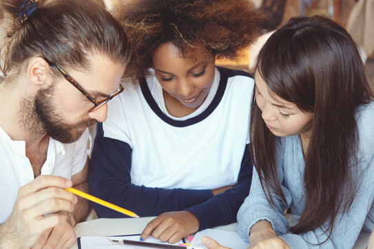 Studierende mit Unterlagen Drei Studierende haben ihre Köpfe über Unterlagen zusammengesteckt.