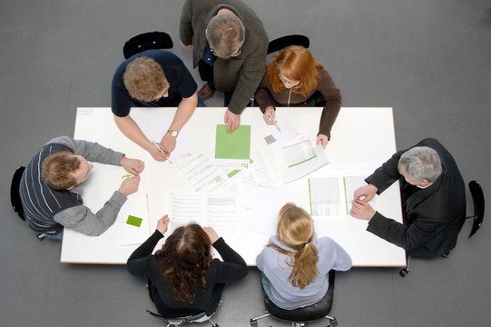 Studierende und Dozierende sitzen gemeinsam an einem Tisch und arbeiten.
